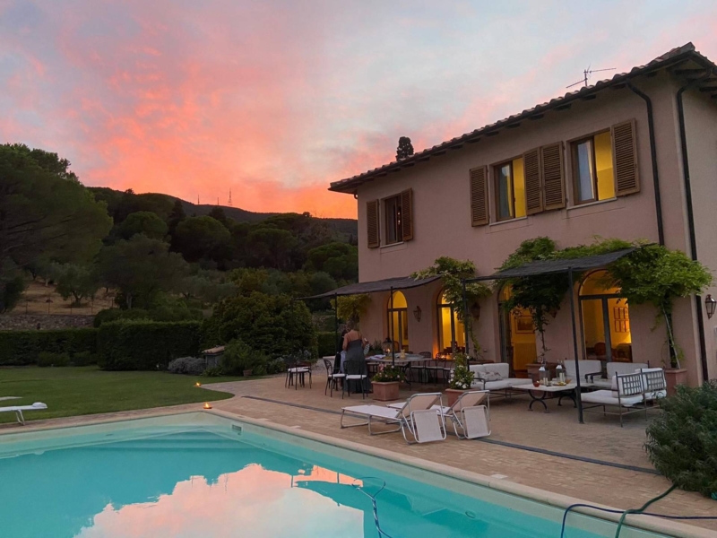 Tuscan villa at sunset with a pool, patio furniture, and lush greenery surrounding the property.