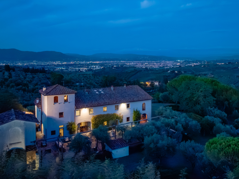 A charming villa at twilight, surrounded by olive trees and rolling hills under a deep blue sky.